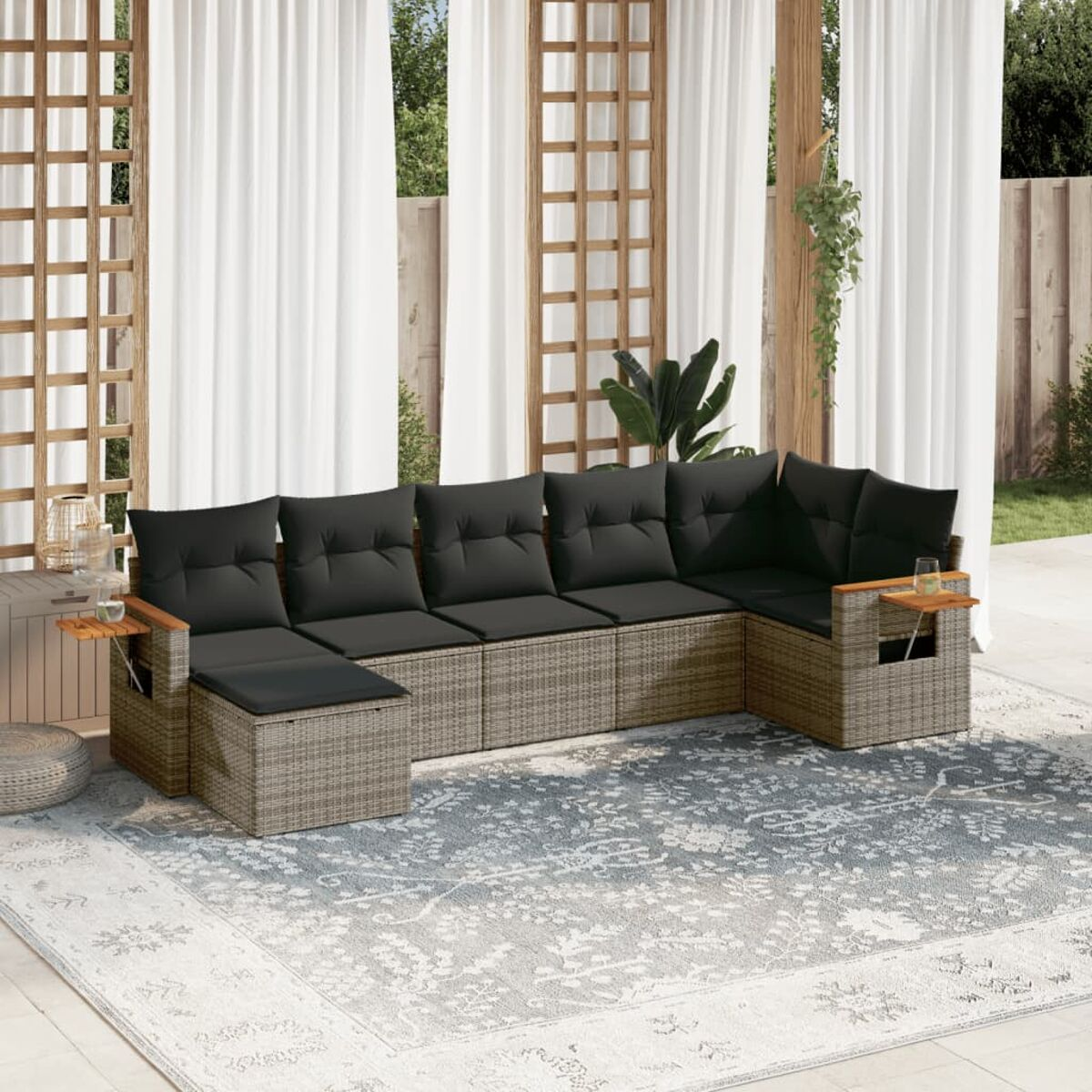 L-förmiges Outdoor-Sofa mit schwarzen Kissen auf einem Teppich. Holzakzente und weiße Vorhänge im Hintergrund.