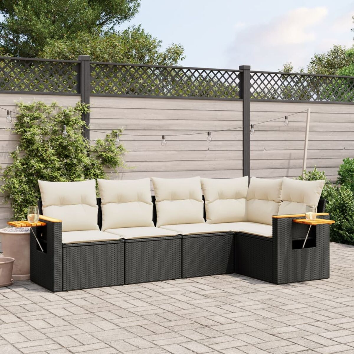 Terrassenmöbel-Set mit schwarzem Korbgeflecht, beigen Kissen und hölzernen Beistelltischen. Pflasterterrasse.