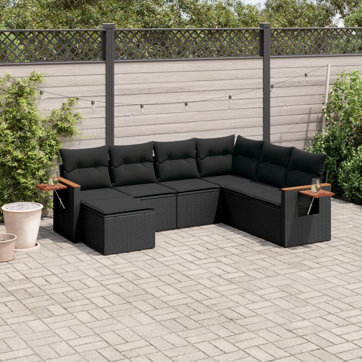 Outdoor-Rattan-Sofagarnitur mit schwarzen Kissen, auf einer Terrasse angeordnet, mit kleinen hölzernen Beistelltischen.