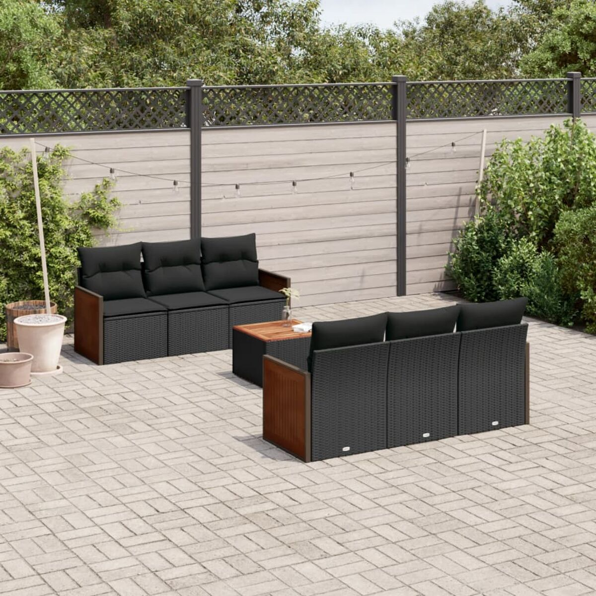 Garten-Set mit schwarzen Kissen, Holzrahmen auf Ziegelpflaster. Hintergrund: Zaun und grüne Bäume.