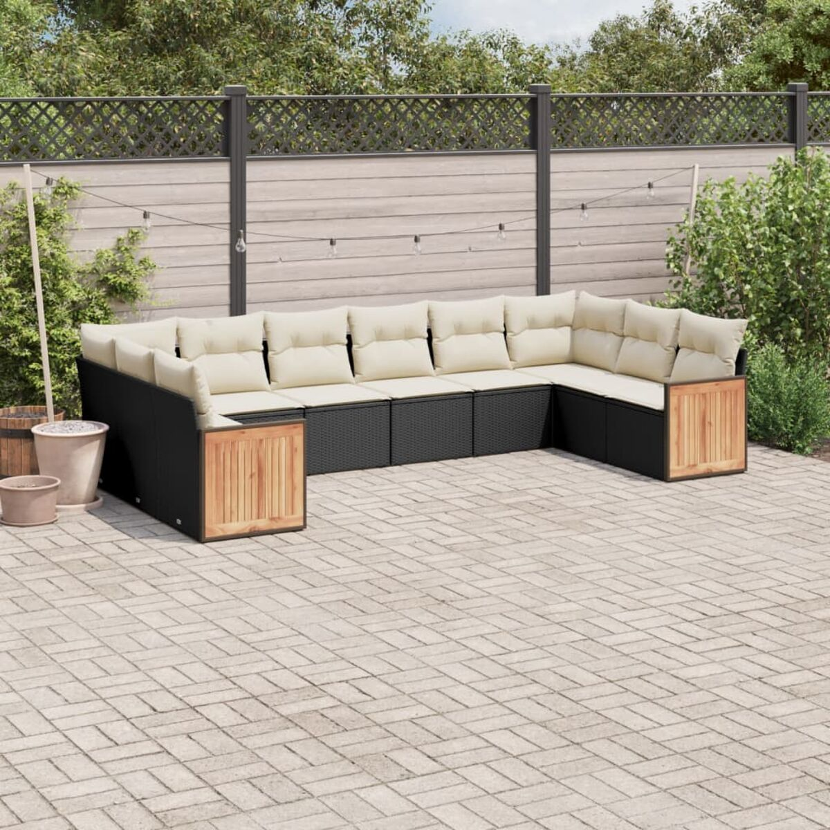 Outdoor-Sitzbereich mit schwarzem Rattan-Sofa und Holzakzenten. Beige Kissen. Ziegel-Terrasse, mit Pflanzen.