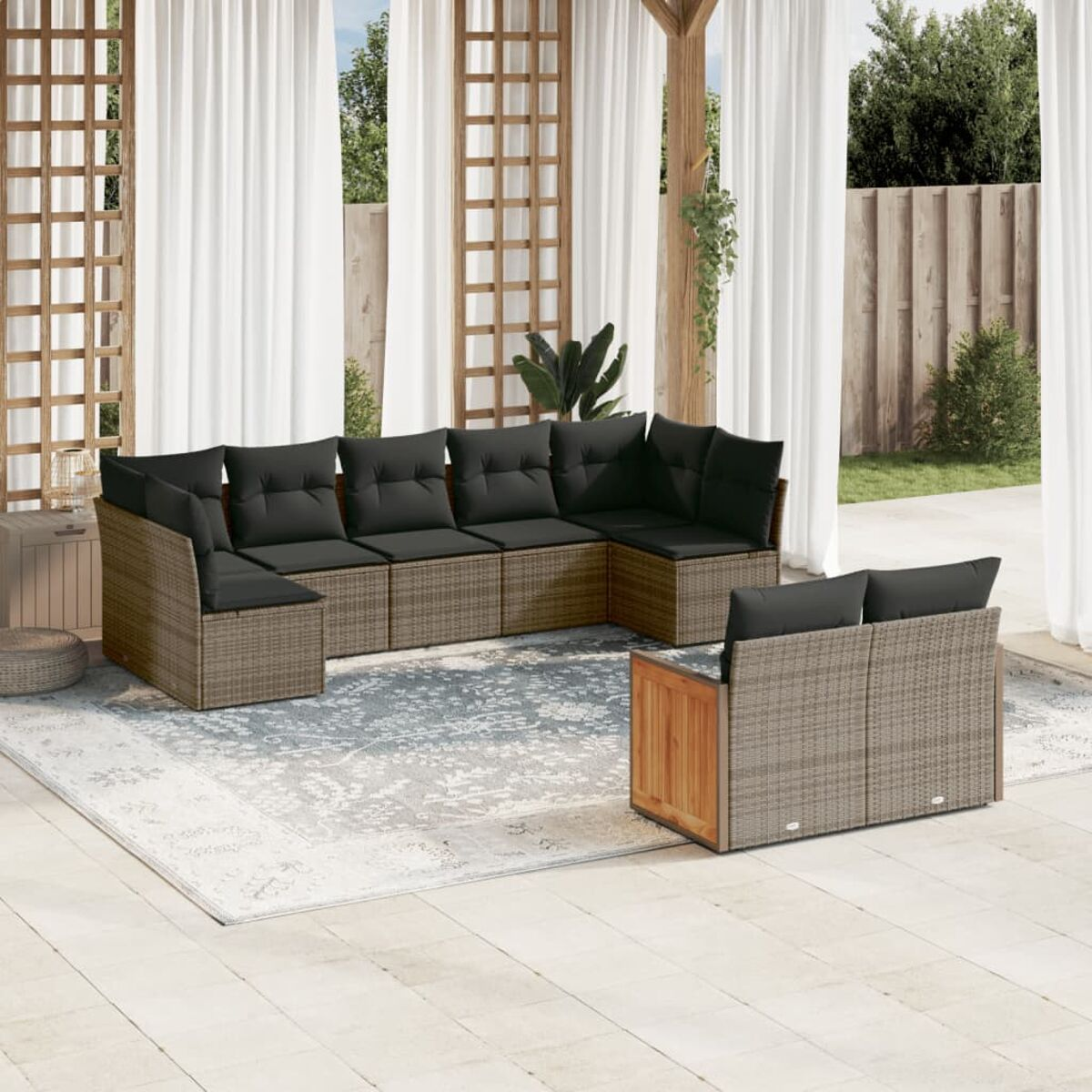 Set divano componibile da esterno, cuscini grigi, struttura in rattan marrone, su un tappeto azzurro chiaro.