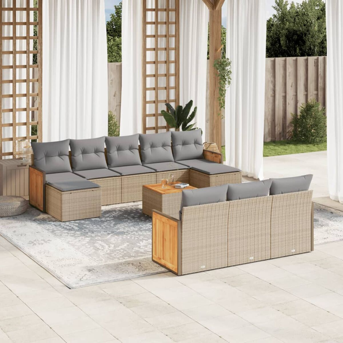 Geflochtenes Terrassenmöbel-Set mit grauen Kissen, einem Tisch und einem Teppich. Weiße Vorhänge und Holzgitter im Hintergrund.