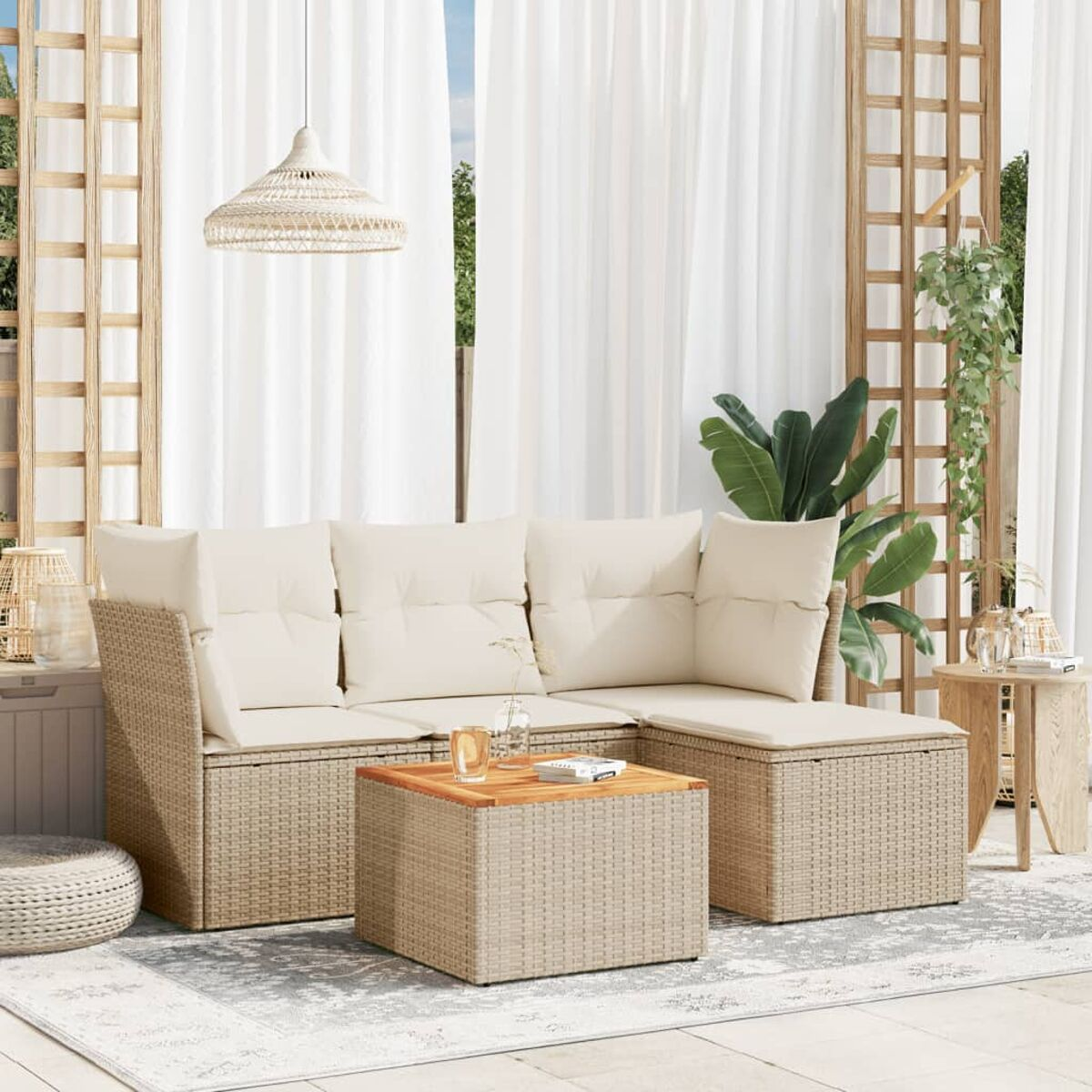 Beiges Rattan-Outdoor-Sofa mit Kissen und einem Couchtisch. Weiße Vorhänge und Pflanzen sichtbar.