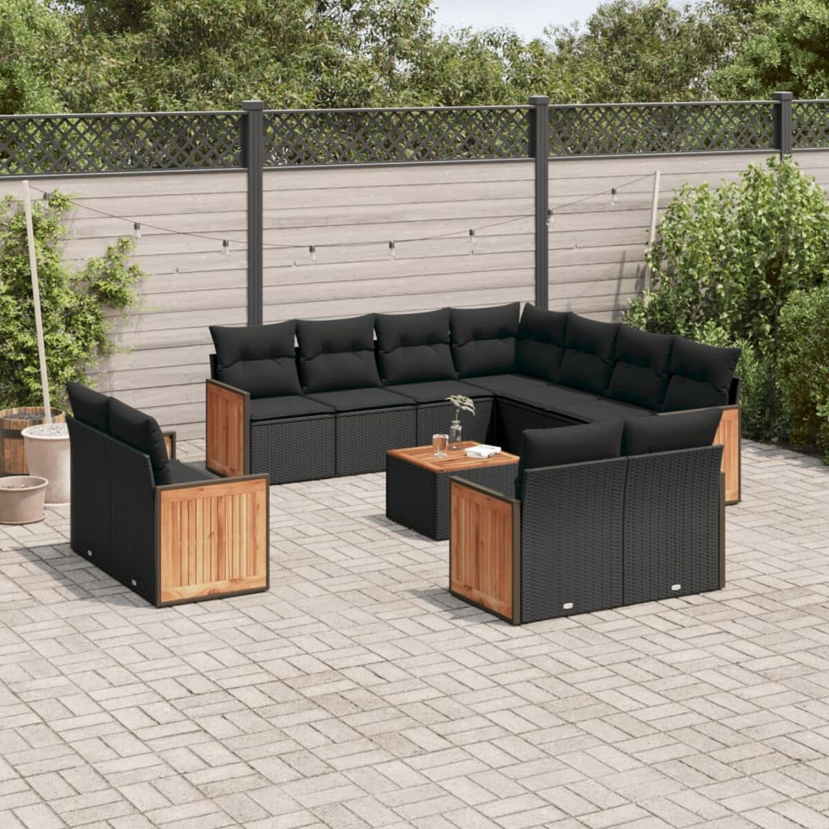 Terrassenset mit schwarzen Kissen. Das Set hat einen Tisch und steht auf gepflasterter Terrasse.