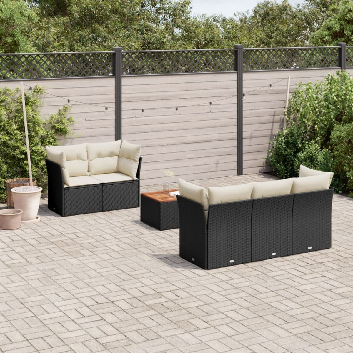 Schwarzes Korbmöbel mit cremefarbenen Kissen, Tisch auf Terrasse mit Zaun und Pflanzen.