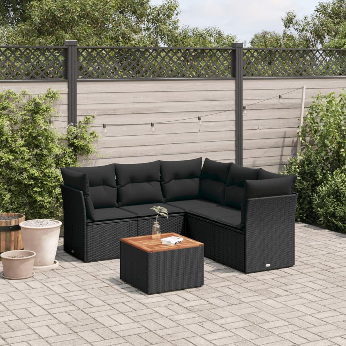 Schwarzes Korbmöbel-Set mit kleinem Tisch auf einer Terrasse. Hintergrund mit Zaun und Pflanzen.