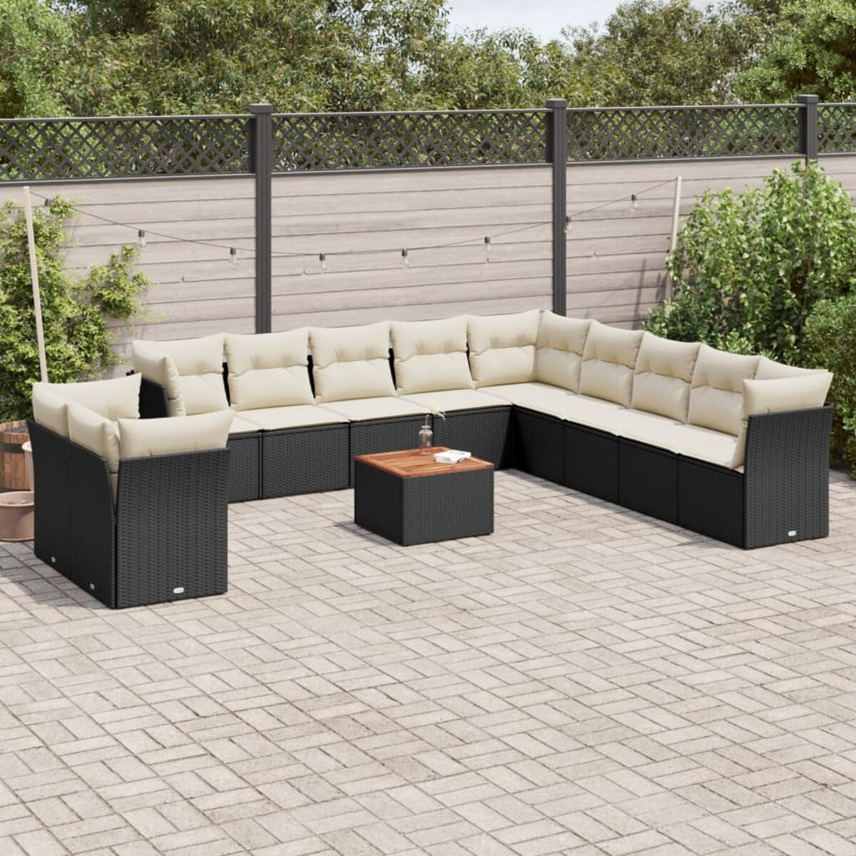 Schwarze Couch mit cremefarbenen Kissen und Holztisch auf Ziegelterrasse mit Zaun und Lichterkette.