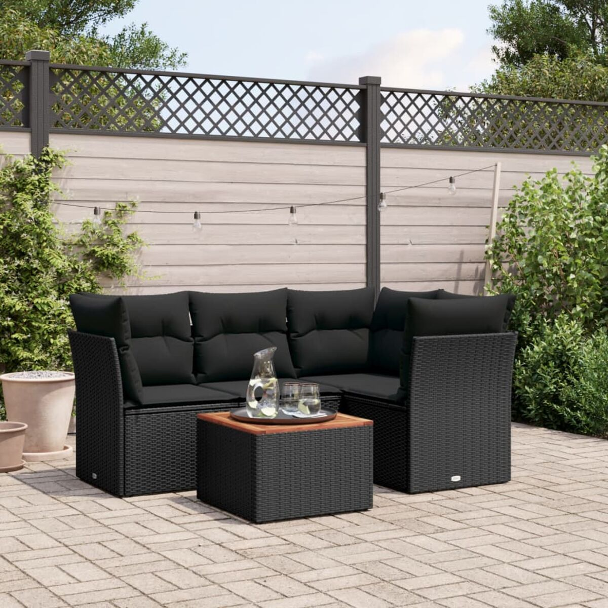 Schwarzes Rattan-Sofaset mit schwarzen Kissen, Couchtisch, auf einer gepflasterten Terrasse.