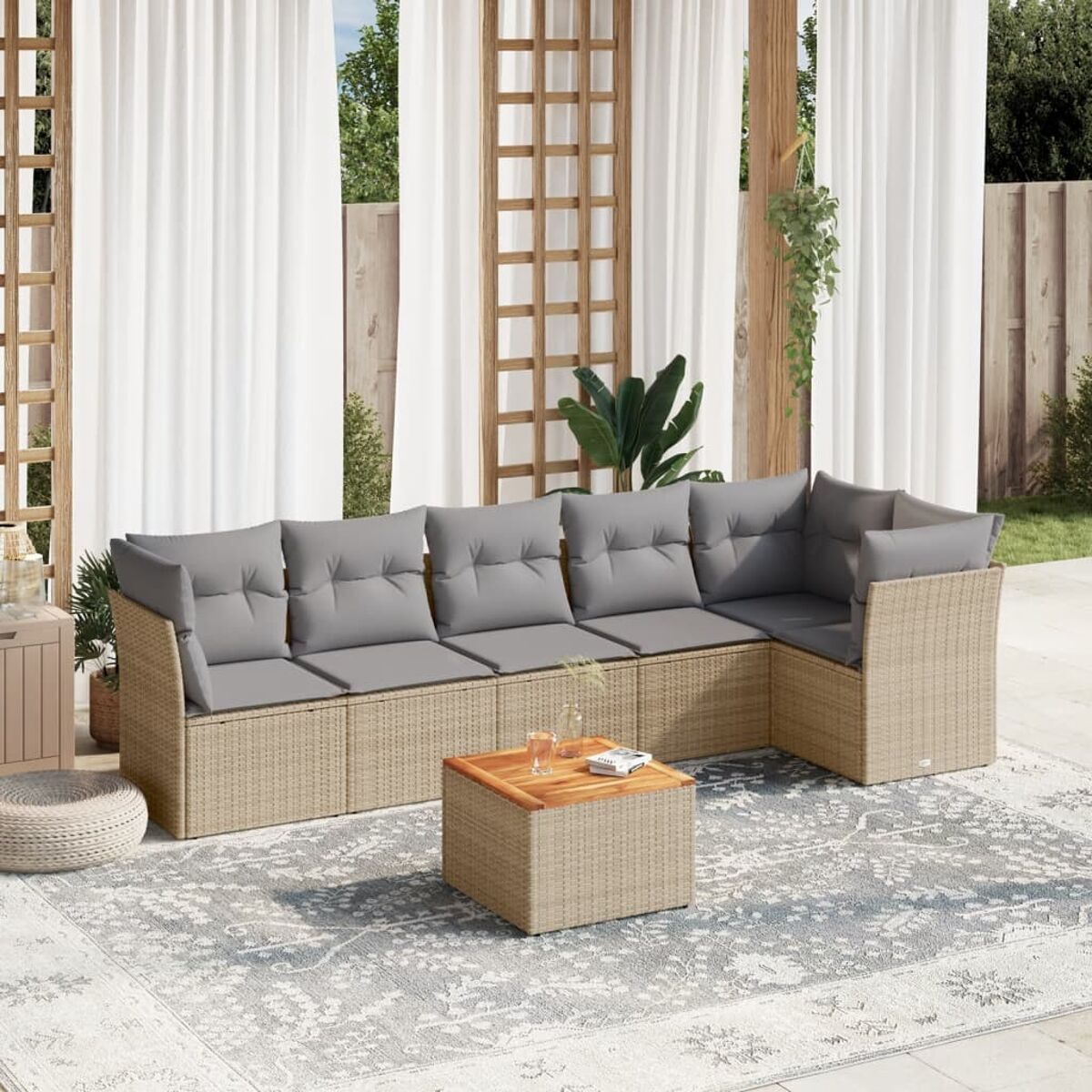 Outdoor-Sofa aus hellbraunem Korbgeflecht mit grauen Kissen, einem Couchtisch und einem gemusterten Teppich.