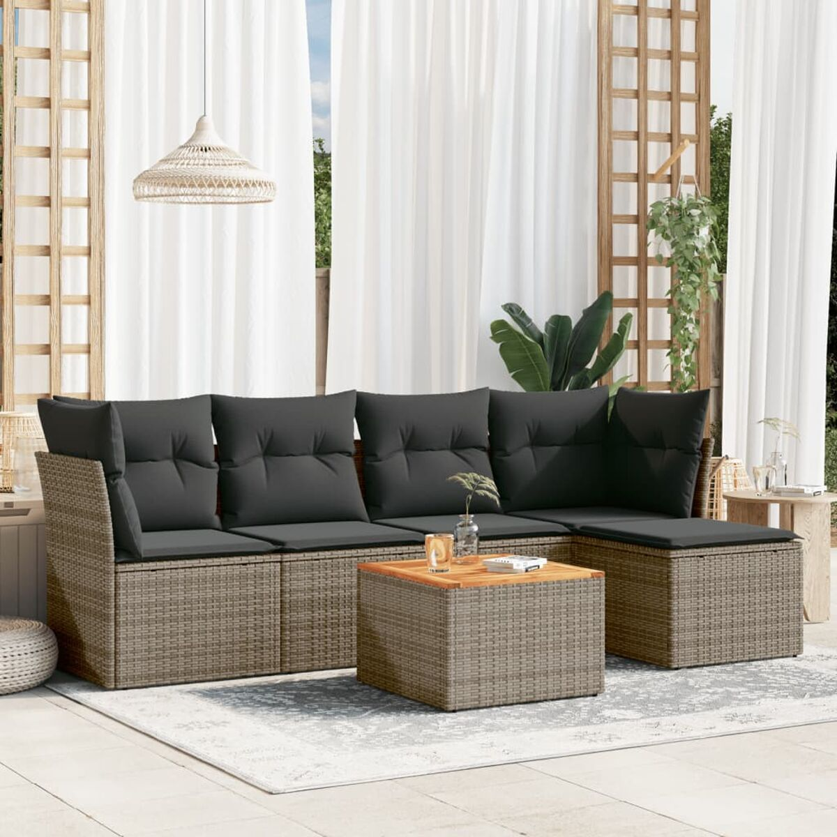 Outdoor-Set: graue Kissen auf Rattan-Sofa und Couchtisch. Vorhänge, Pflanze und Hängeleuchte im Hintergrund.