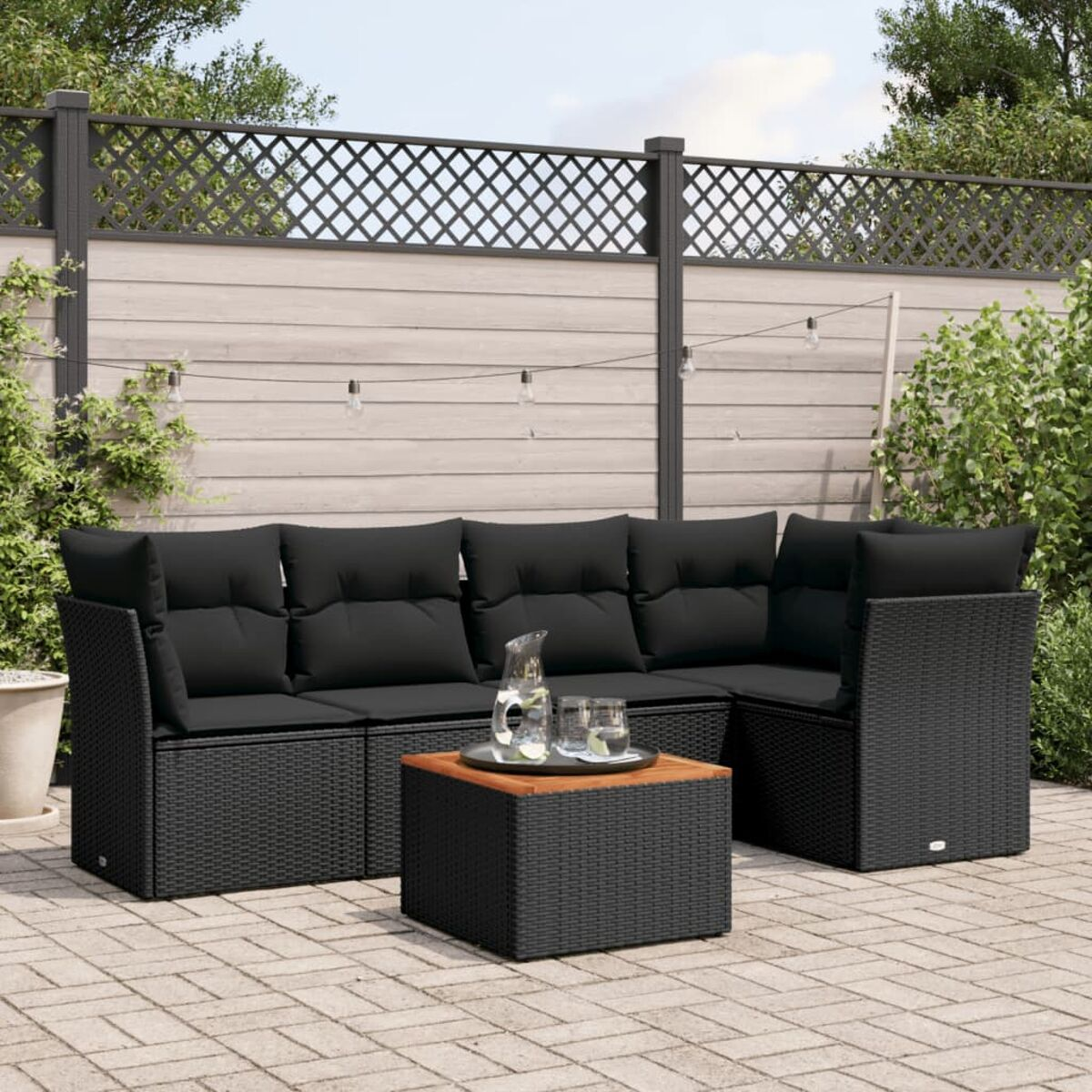 Schwarzes Outdoor-Ecksofa auf Terrasse. Schwarze Kissen, quadratischer Tisch. Sonnig.