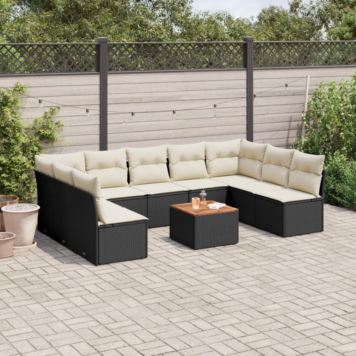 Outdoor-Ecksofa-Set mit cremefarbenen Kissen, schwarzem Rahmen und einem Holztisch. Zaun und Lichter im Hintergrund.
