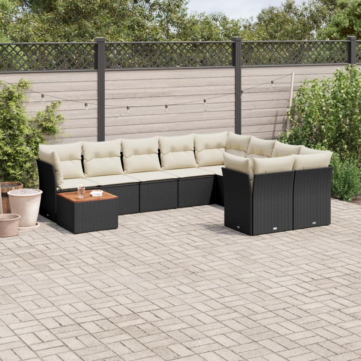 Ein schwarzes Rattan-Ecksofa-Set mit cremefarbenen Kissen. Der Hintergrund ist eine gepflasterte Terrasse.