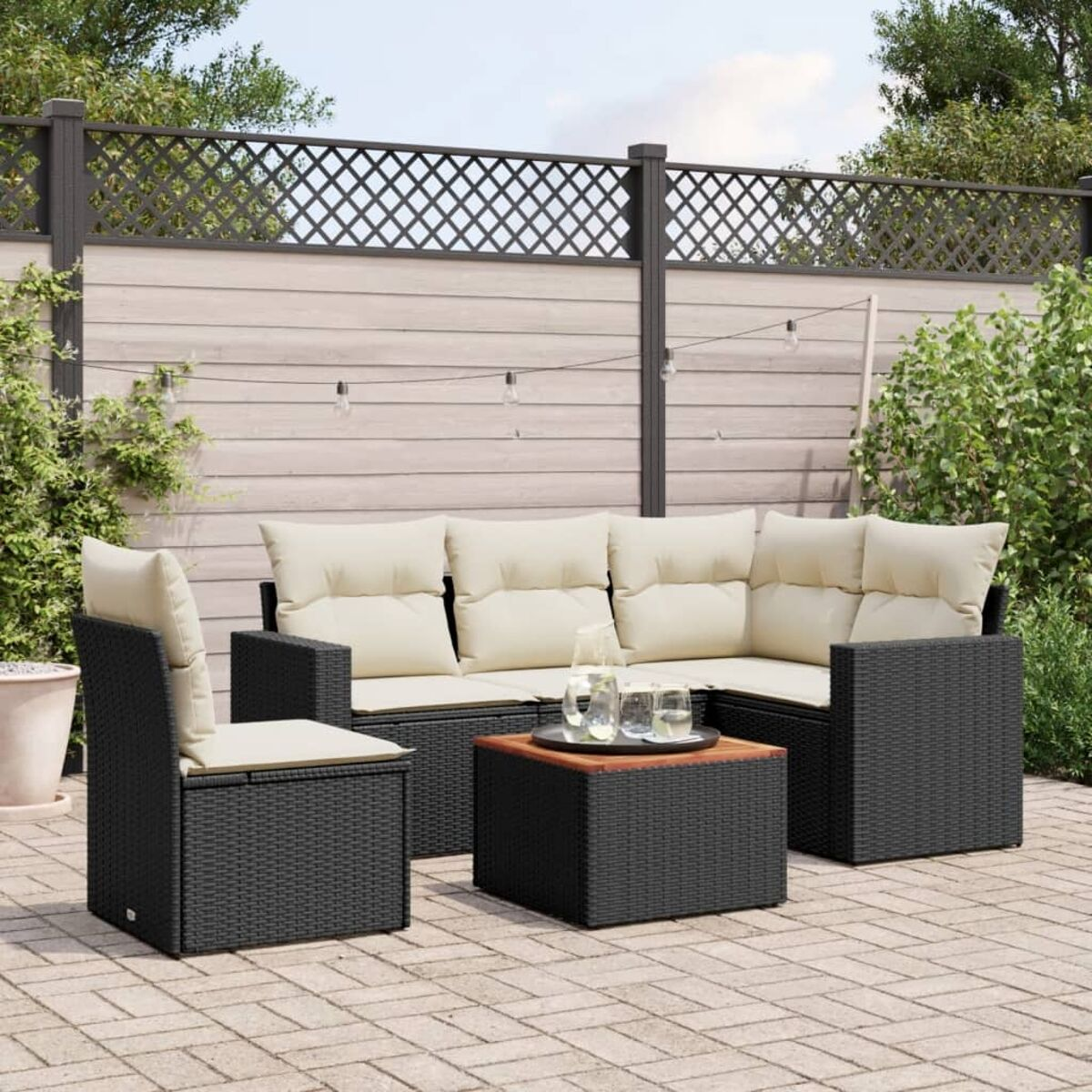 Schwarzes Rattan-Sofaset mit cremefarbenen Kissen und einem Couchtisch auf einer Terrasse.