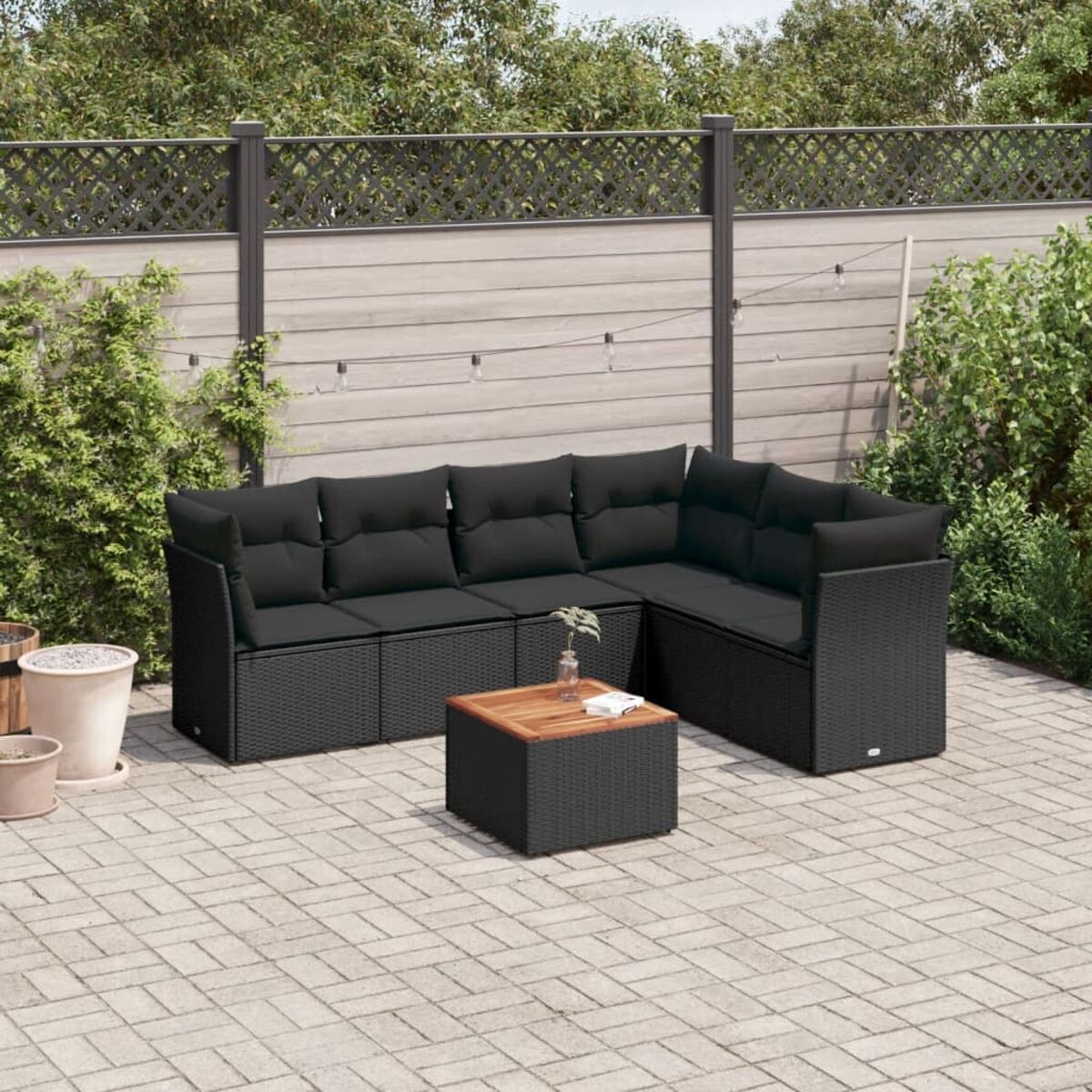 Schwarzes Korbmöbel-Set mit Sofa und Tisch. Auf einer Terrasse mit Grün.