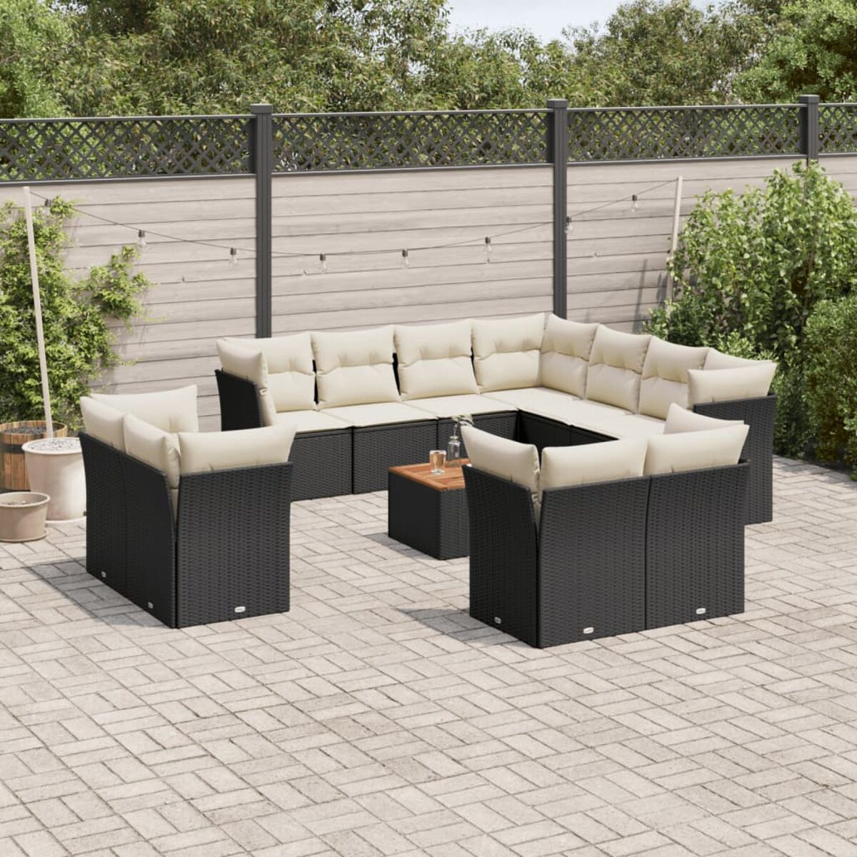 Ein schwarzes Rattan-Ecksofa-Set mit cremefarbenen Kissen. Der Hintergrund ist eine gepflasterte Terrasse.