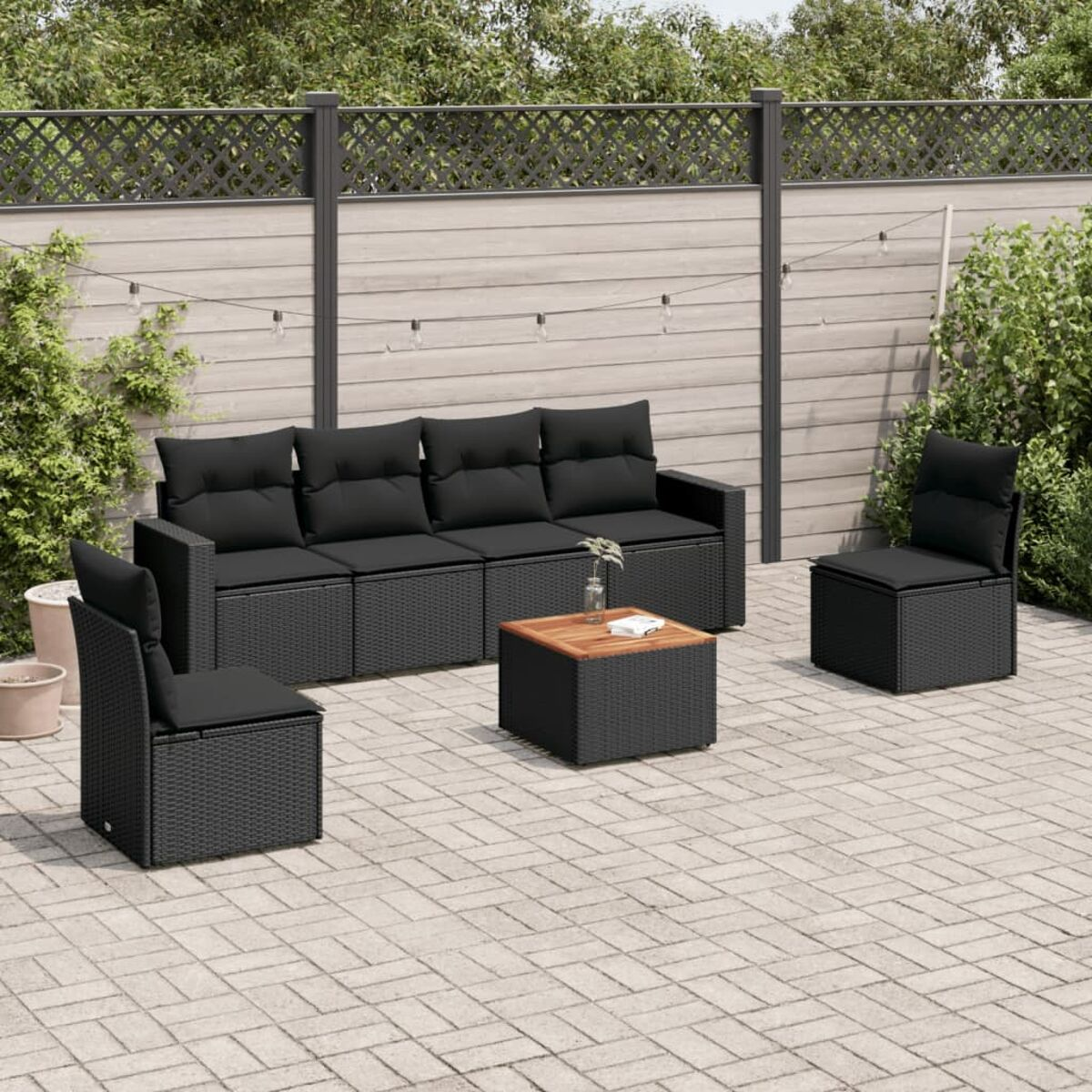 Ein schwarzes Sitzgruppen-Set für den Außenbereich mit schwarzen Kissen, einem kleinen Tisch und einer Backsteinterrasse.