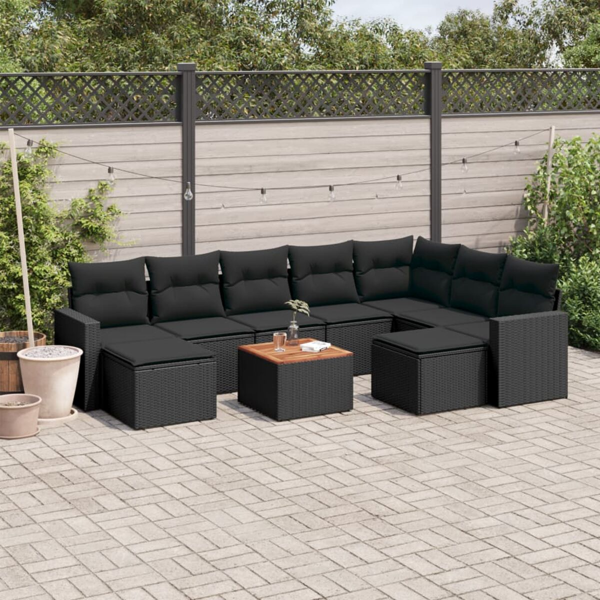 Ein Ecksofa mit schwarzen Kissen und Korbgeflecht. Ein quadratischer Tisch davor. Szene draußen mit Pflastersteinen.