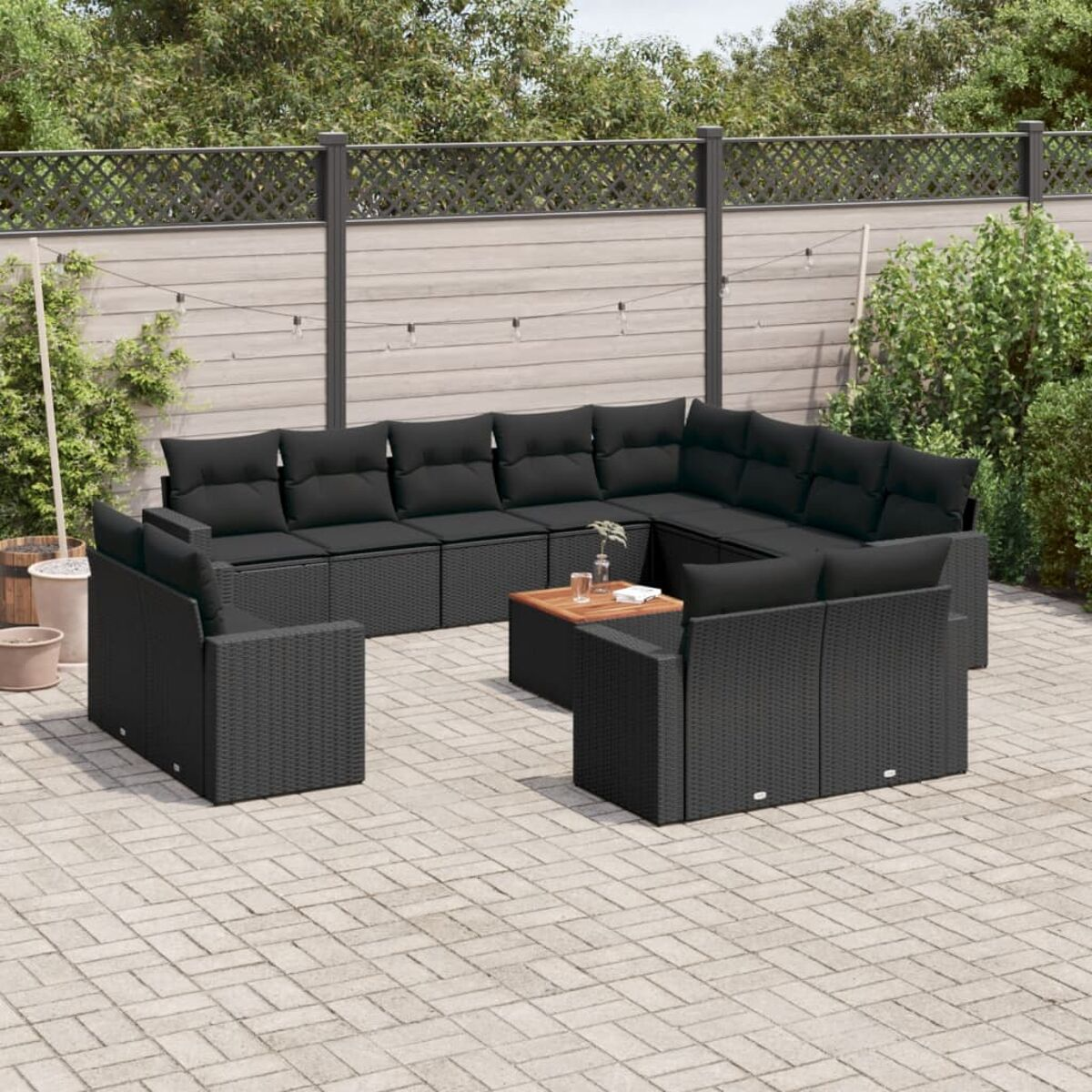 Schwarzes Outdoor-Geflechtmöbel-Set mit Kissen und einem Holztisch auf einer gepflasterten Terrasse.