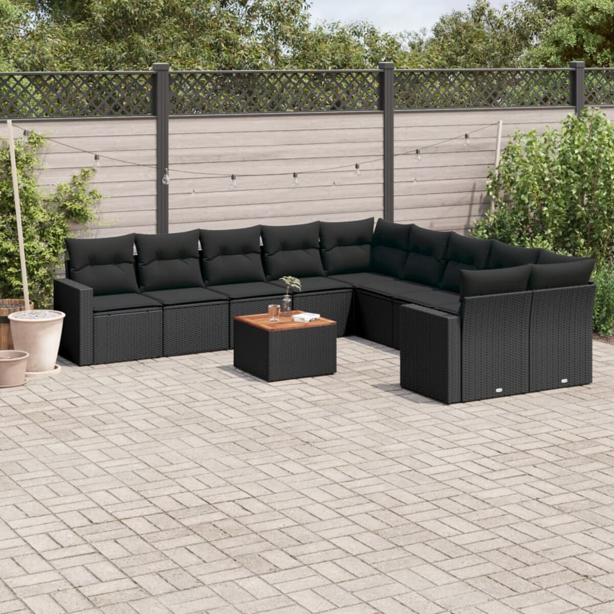 Schwarzes Outdoor-Sofaset mit Kissen und einem Tisch. Umgeben von Zaun und Pflanzen.