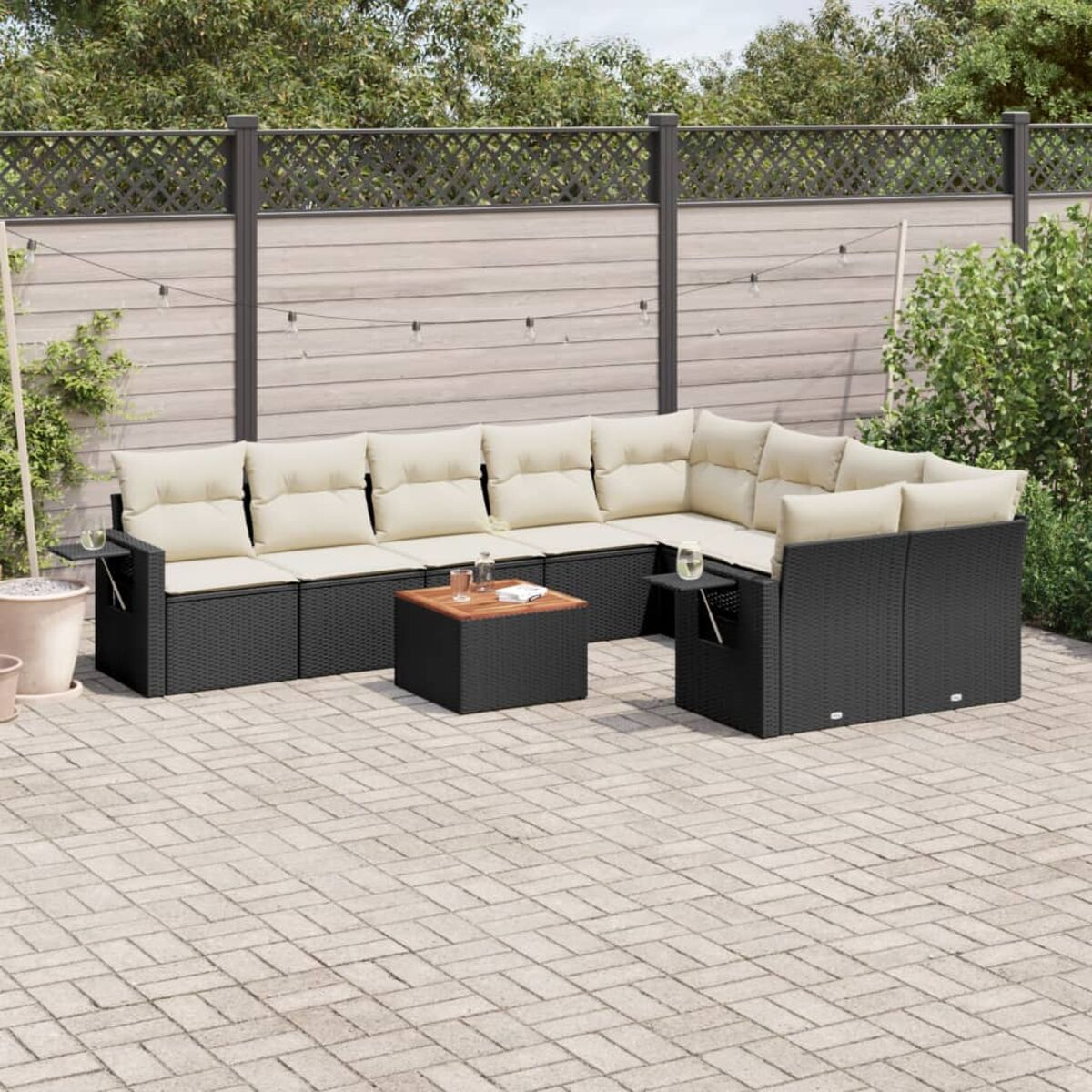 Schwarzes Outdoor-Ecksofa mit beigen Kissen, kleinem Tisch, Backstein-Terrasse, Grün im Hintergrund.