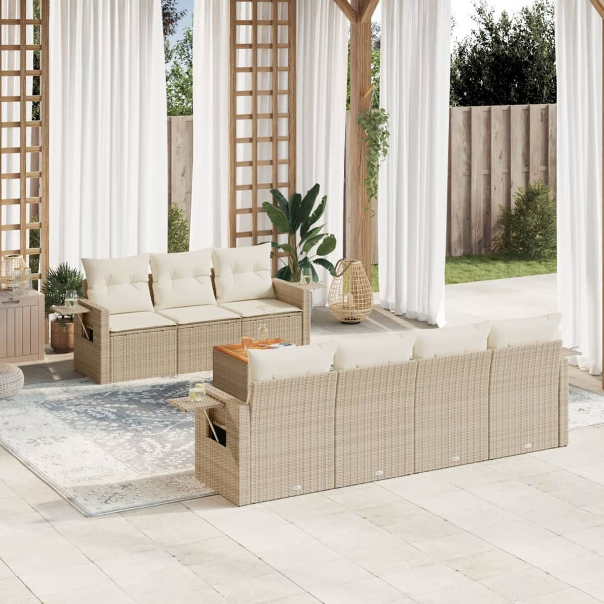 Divano in vimini beige con cuscini color crema, tavolino e tappeto su un patio con tende bianche.