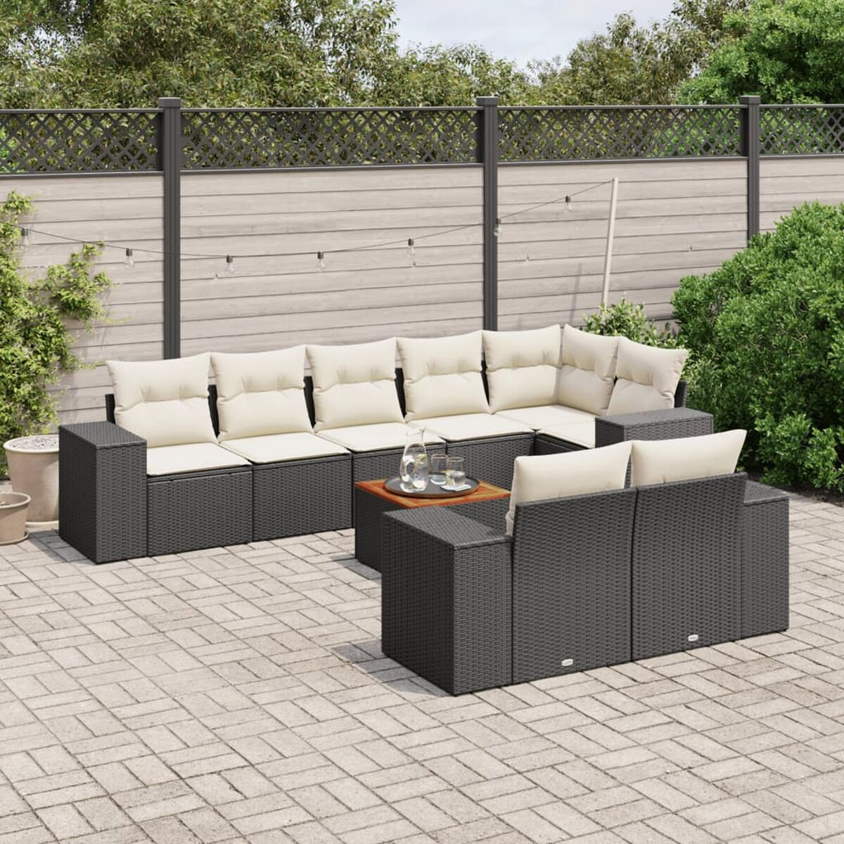 Schwarzes Ecksofa aus Rattan, cremefarbene Kissen, Couchtisch und gepflasterte Terrasse.
