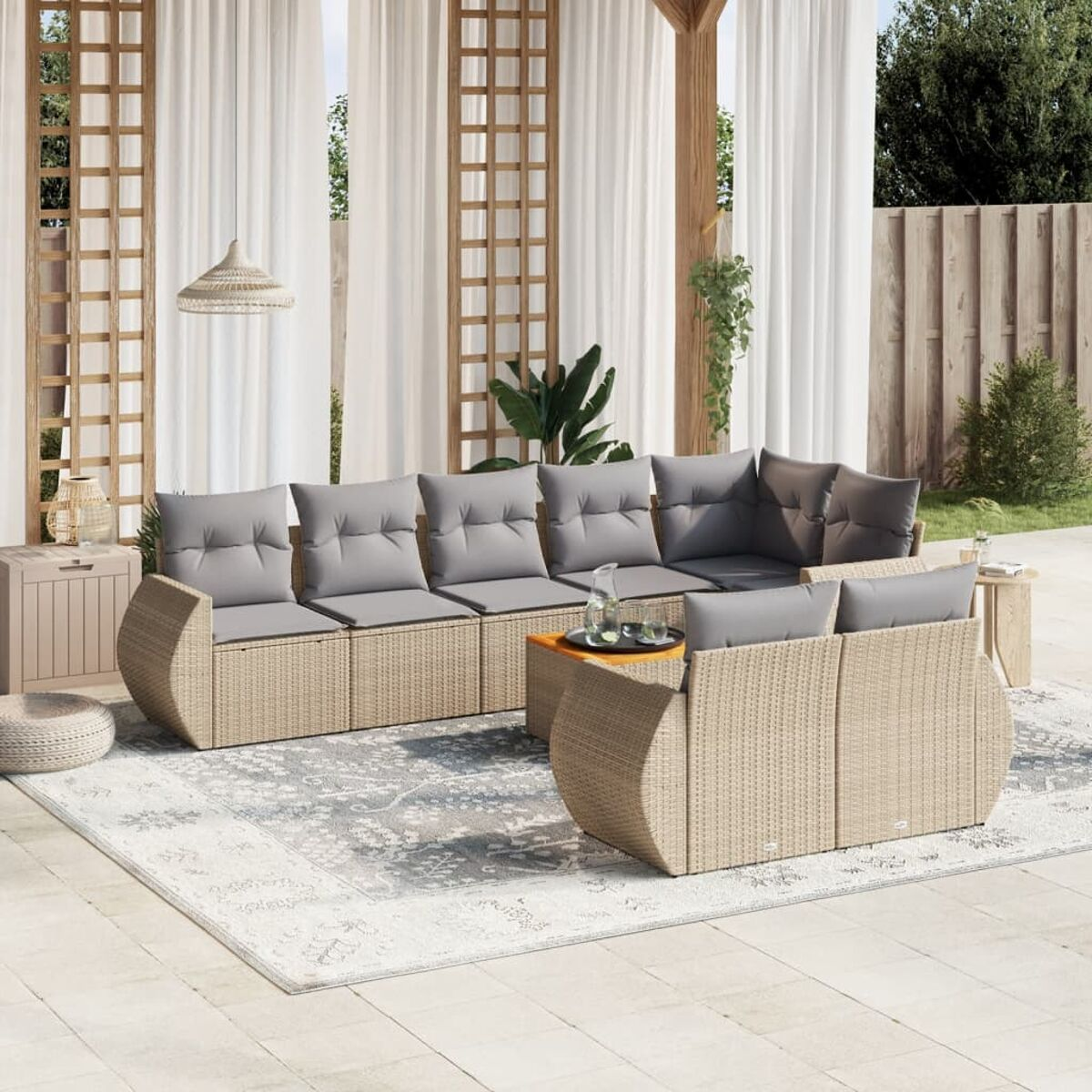 Outdoor-Wicker-Sofa mit grauen Kissen. Ein runder Couchtisch mit Tablett steht auf einem Teppich. Weiße Vorhänge im Hintergrund.