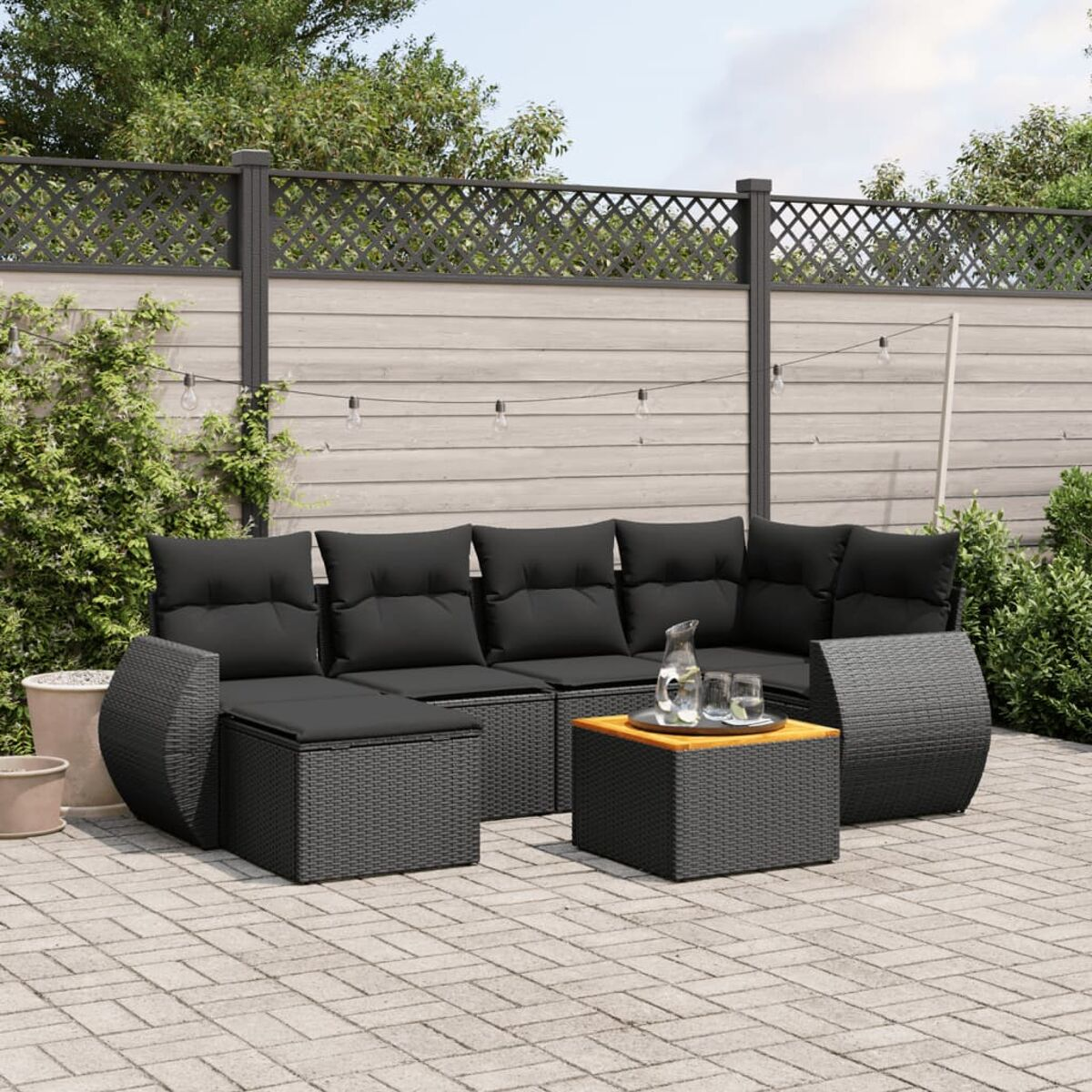 Schwarzes Rattan-Ecksofa mit Kissen, Couchtisch und anderen Möbeln auf einer Backstein-Terrasse.
