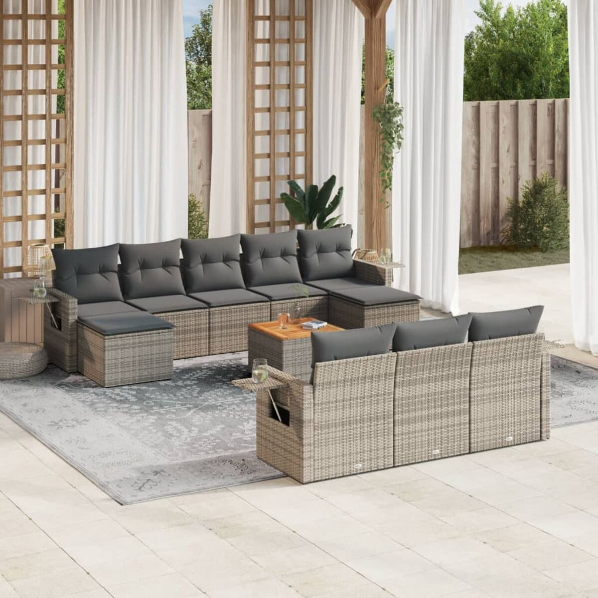Outdoor-Ecksofa-Set mit grauen Kissen, kleinem Tisch, auf einem gemusterten Teppich, mit weißen Vorhängen.