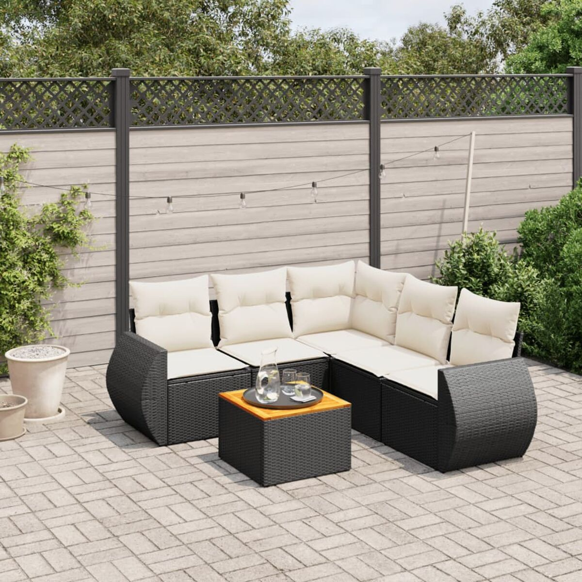 Schwarzes Outdoor-Ecksofa aus Rattan mit cremefarbenen Kissen und Holztisch auf Ziegelterrasse.