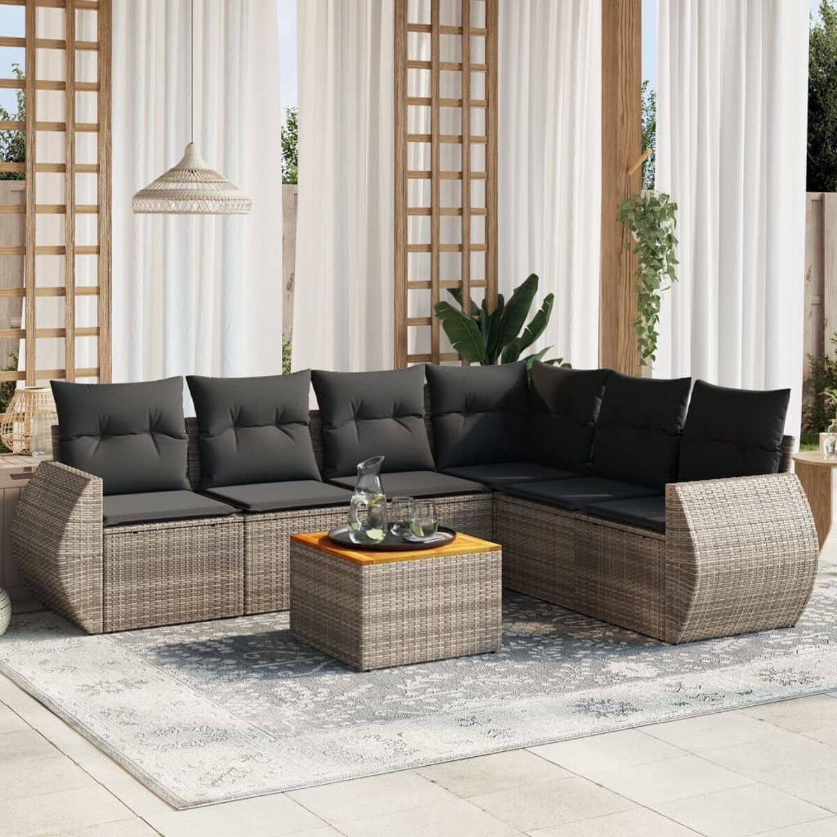 Geflochtenes Ecksofa mit dunkelgrauen Kissen und Couchtisch auf einem gemusterten Teppich, in der Nähe von Vorhängen.