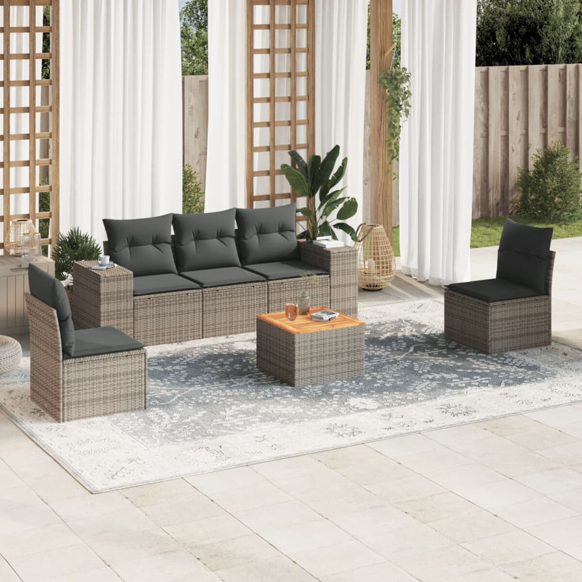 Gartenmöbel: Korbsessel, Couch, Tisch. Graue Kissen, Teppich. Außenbereich mit Vorhängen und Pflanzen.
