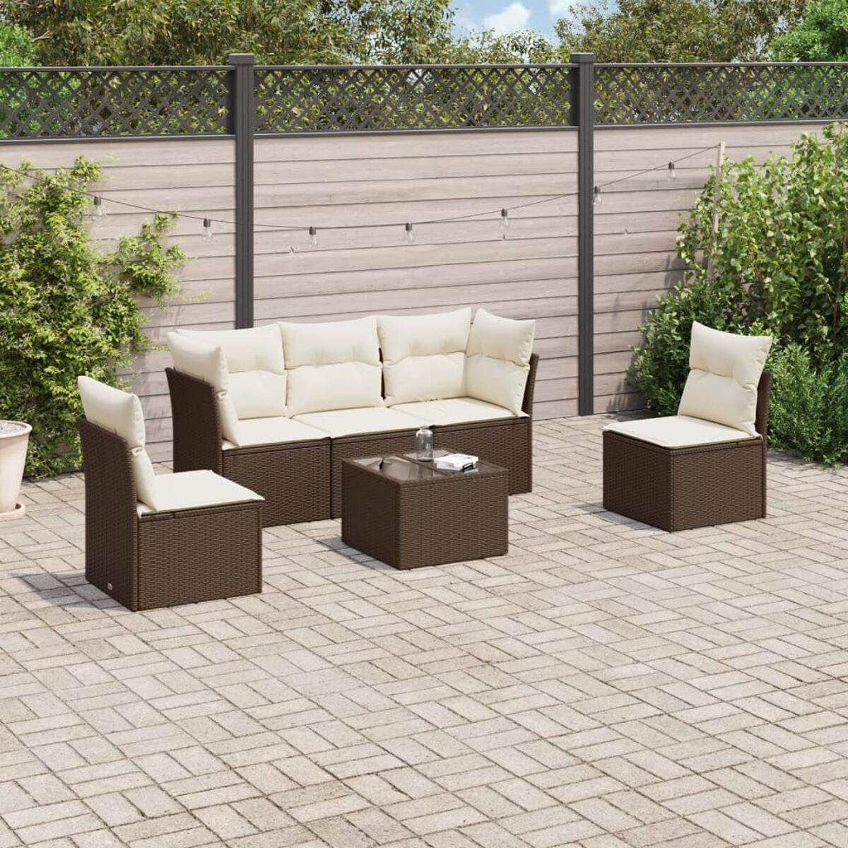 Set di divani in rattan marrone con cuscini color crema e tavolo con piano in vetro.