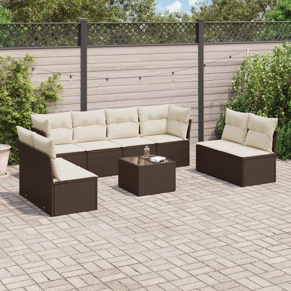 Set patio con divani in vimini marroni e cuscini color crema su un patio in mattoni con una recinzione.