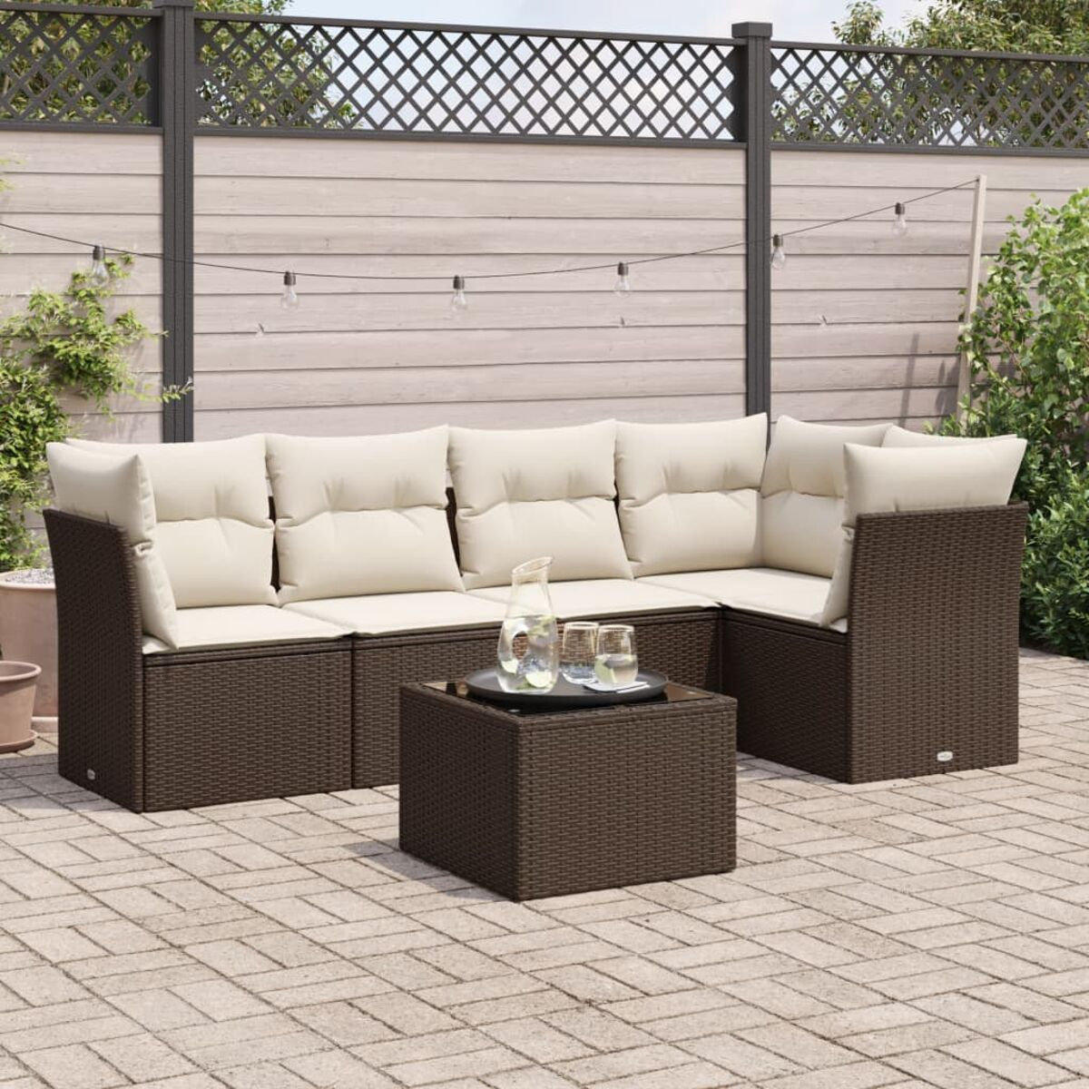 Divano componibile in vimini marrone scuro con cuscini color crema e tavolo con bevande su patio in pietra.