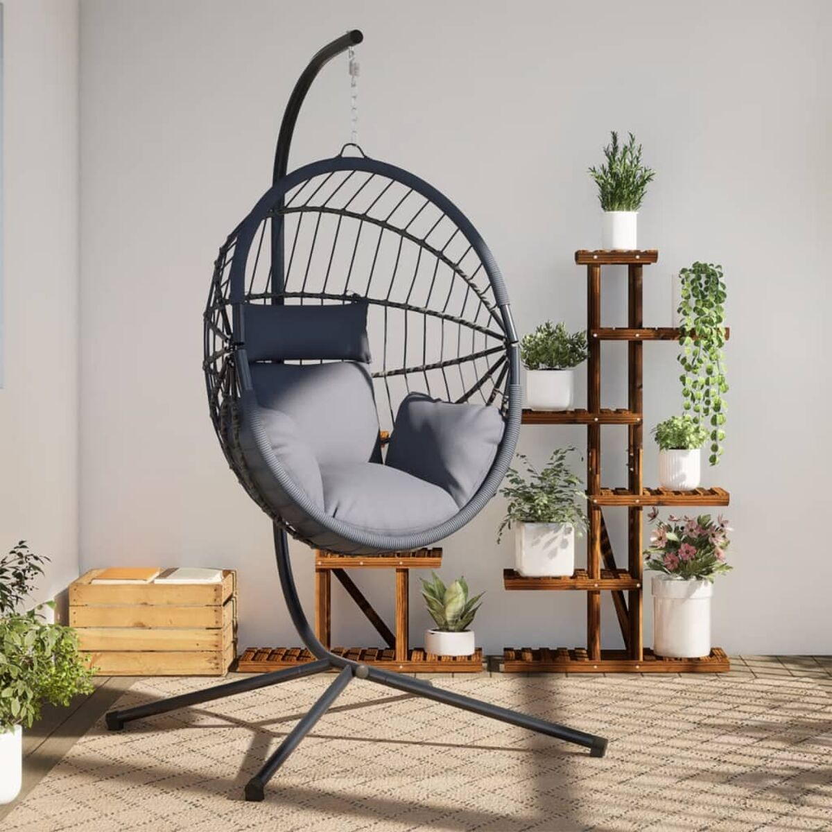 Sedia a uovo sospesa con cuscino grigio, piante in vaso e supporto in legno su patio.
