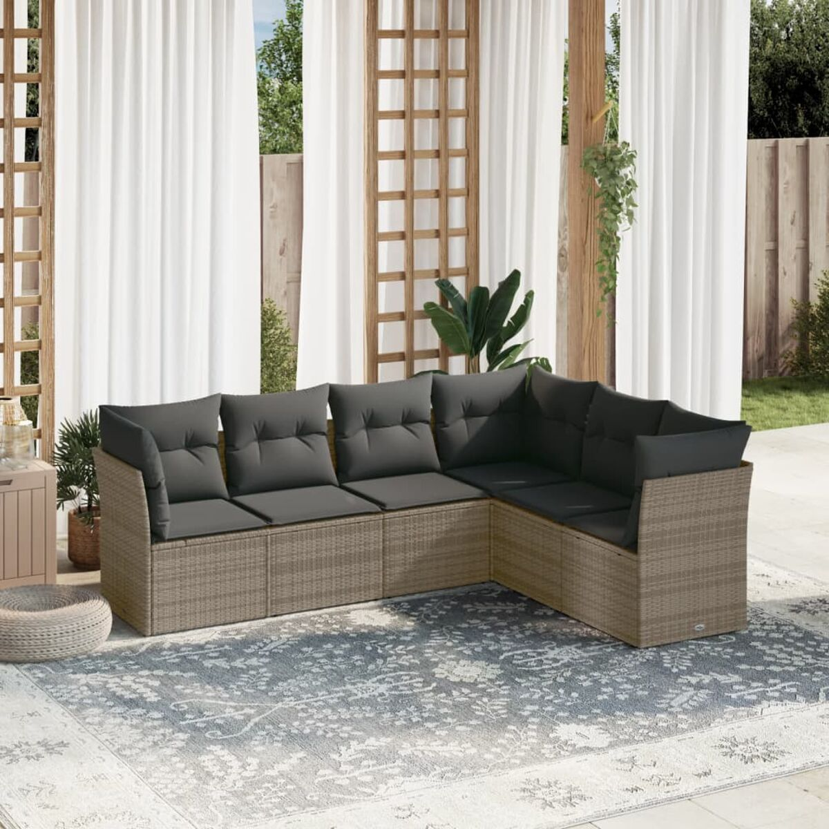 Eck-Rattansofa mit grauen Kissen auf einem gemusterten Teppich. Enthält einen kleinen Tisch. Bäume und Holzzaun im Hintergrund.