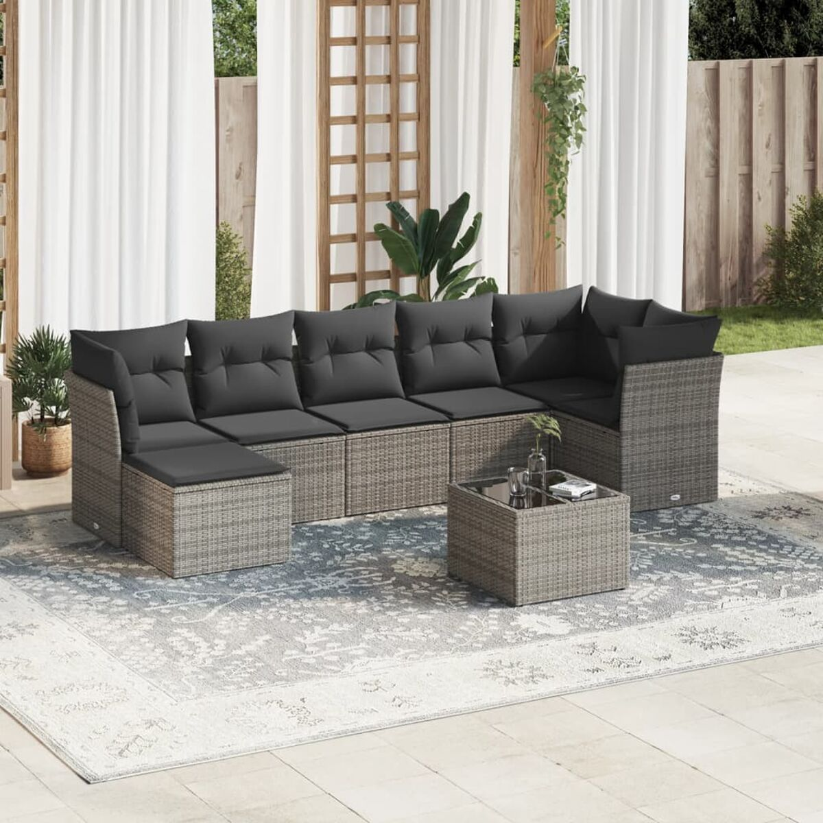 Ein graues Rattan-Gartenmöbelset mit dunkelgrauen Kissen, einem Couchtisch und einem gemusterten Teppich.