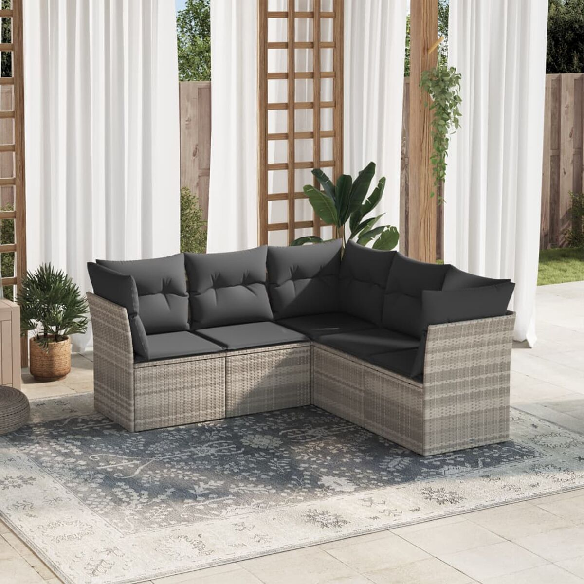 Graues Ecksofa aus Korbgeflecht mit dunkelgrauen Kissen und einem kleinen Tisch auf einem Teppich. Hintergrund ist eine Holzpergola.