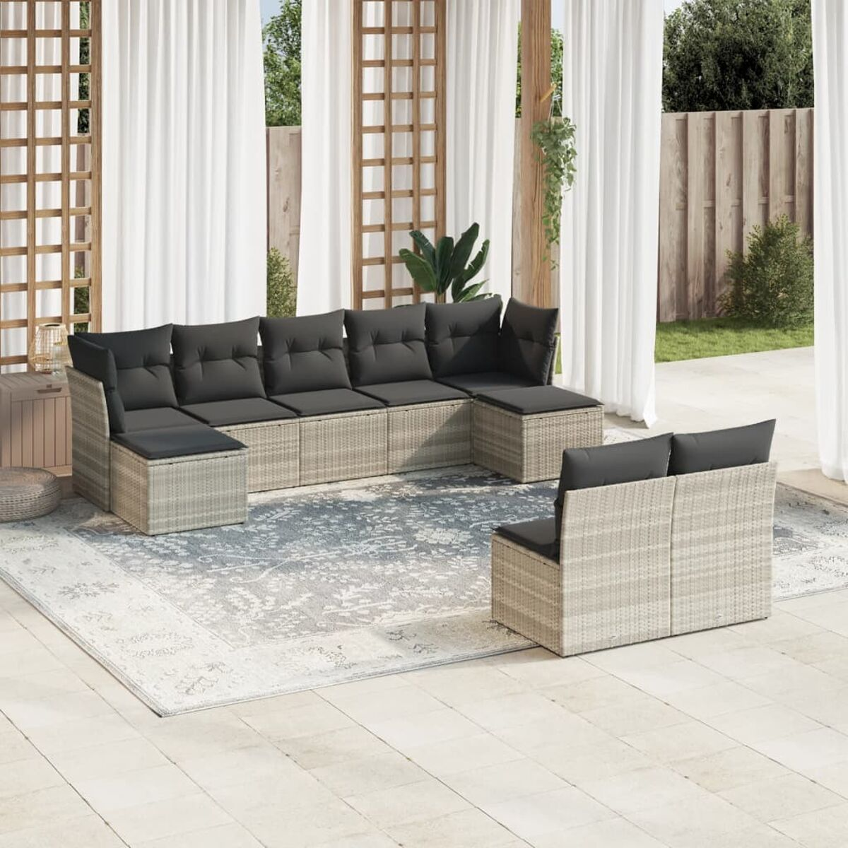 Hellgraues Outdoor-Ecksofa aus Korbgeflecht mit grauen Kissen und einem Teppich, auf einer Terrasse mit weißen Vorhängen.