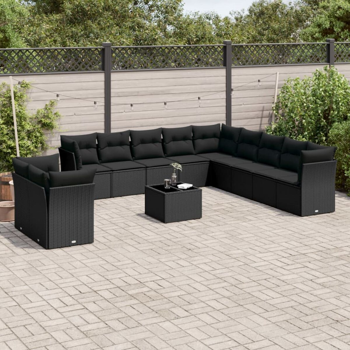 Schwarzes Rattan-Gartenmöbel-Set mit schwarzen Kissen und einer Ziegel-Terrasse.