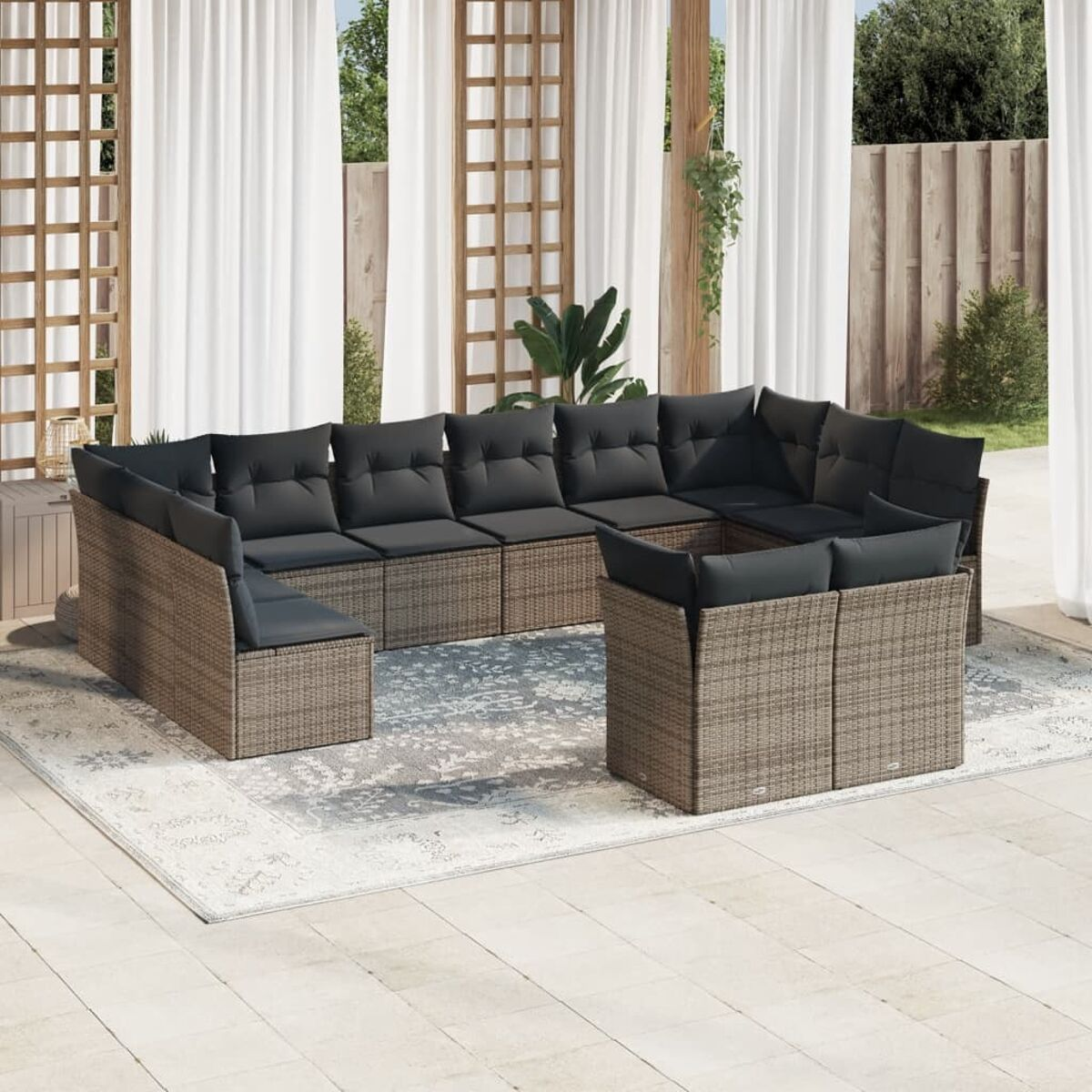 Graues Outdoor-Sofa mit dunkelgrauen Kissen und einem kleinen Tisch auf einer gepflasterten Terrasse. Weiße Vorhänge im Hintergrund.