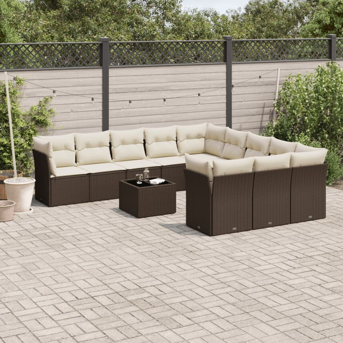 Braunes Korbmöbel mit cremefarbenen Kissen, Tisch auf Terrasse mit Zaun und Pflanzen.