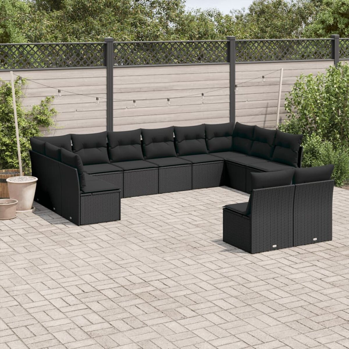 Gartenmöbel-Set. Ein großes U-förmiges schwarzes Sofa mit einem einzelnen Stuhl. Schwarze Kissen und eine Ziegelterrasse.