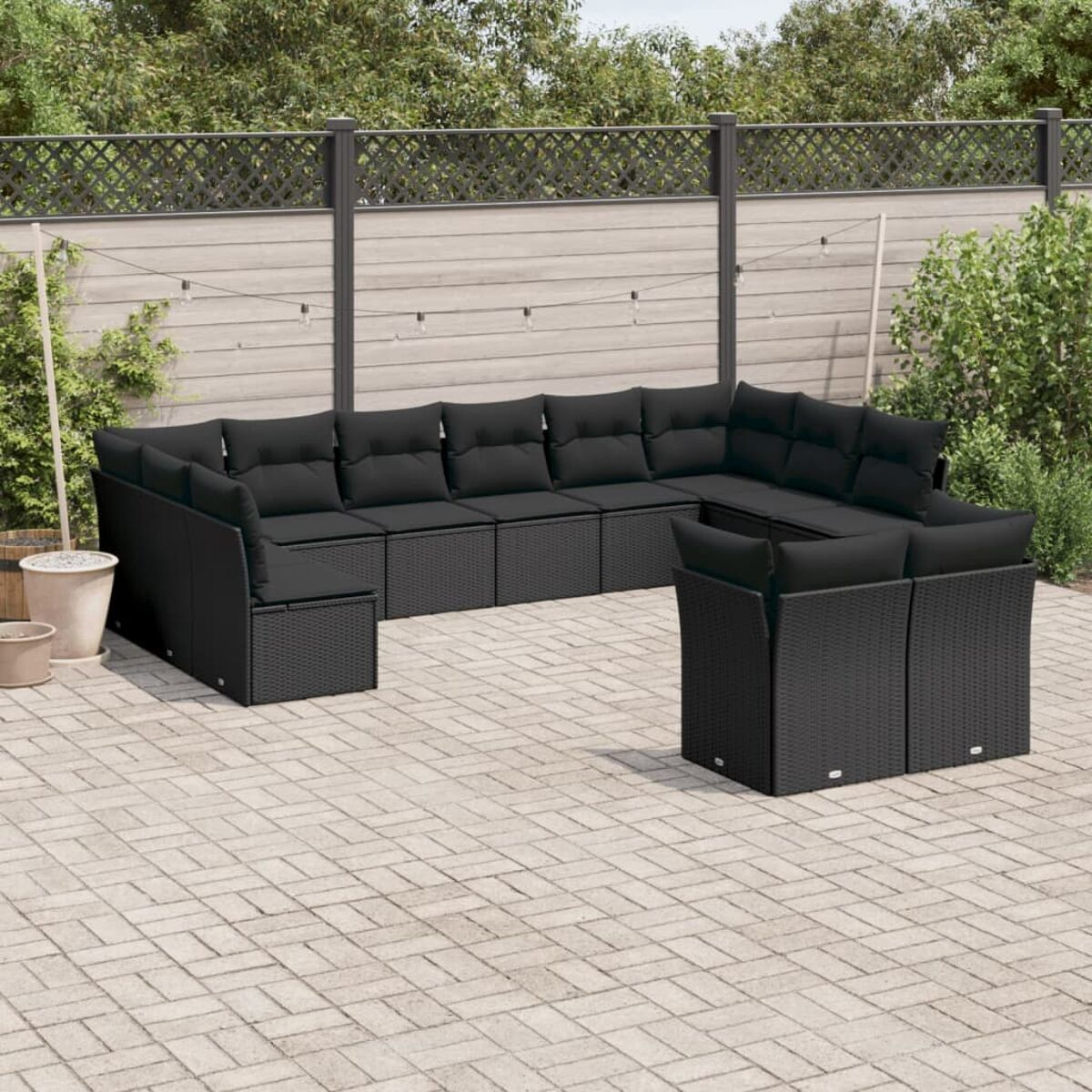 Schwarzes Rattan-Ecksofa-Set in einer Ziegelsteinterrasse mit dunklen Kissen.