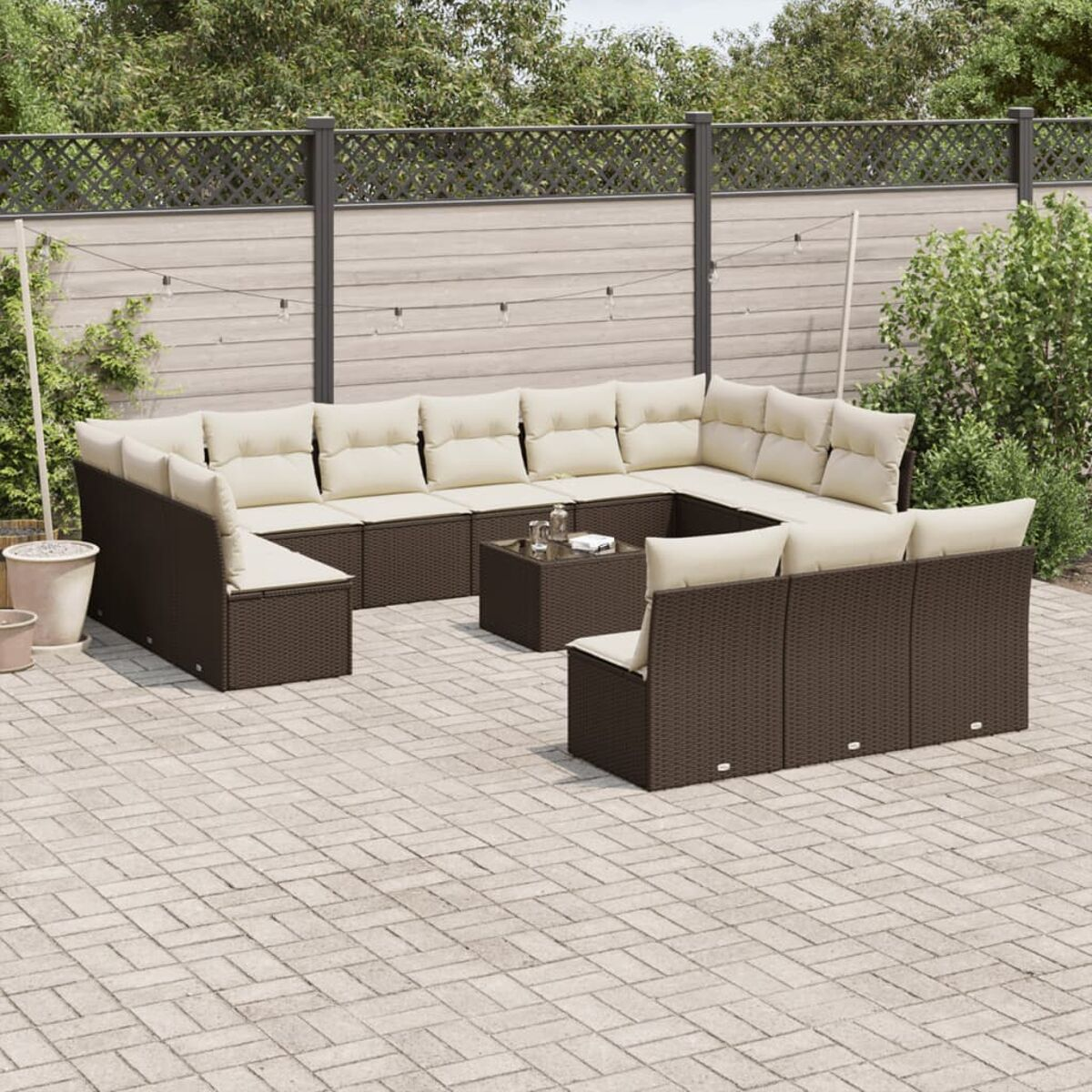 Set divani da esterno in rattan marrone con cuscini beige. Tavolino su un patio. Piante in vaso.