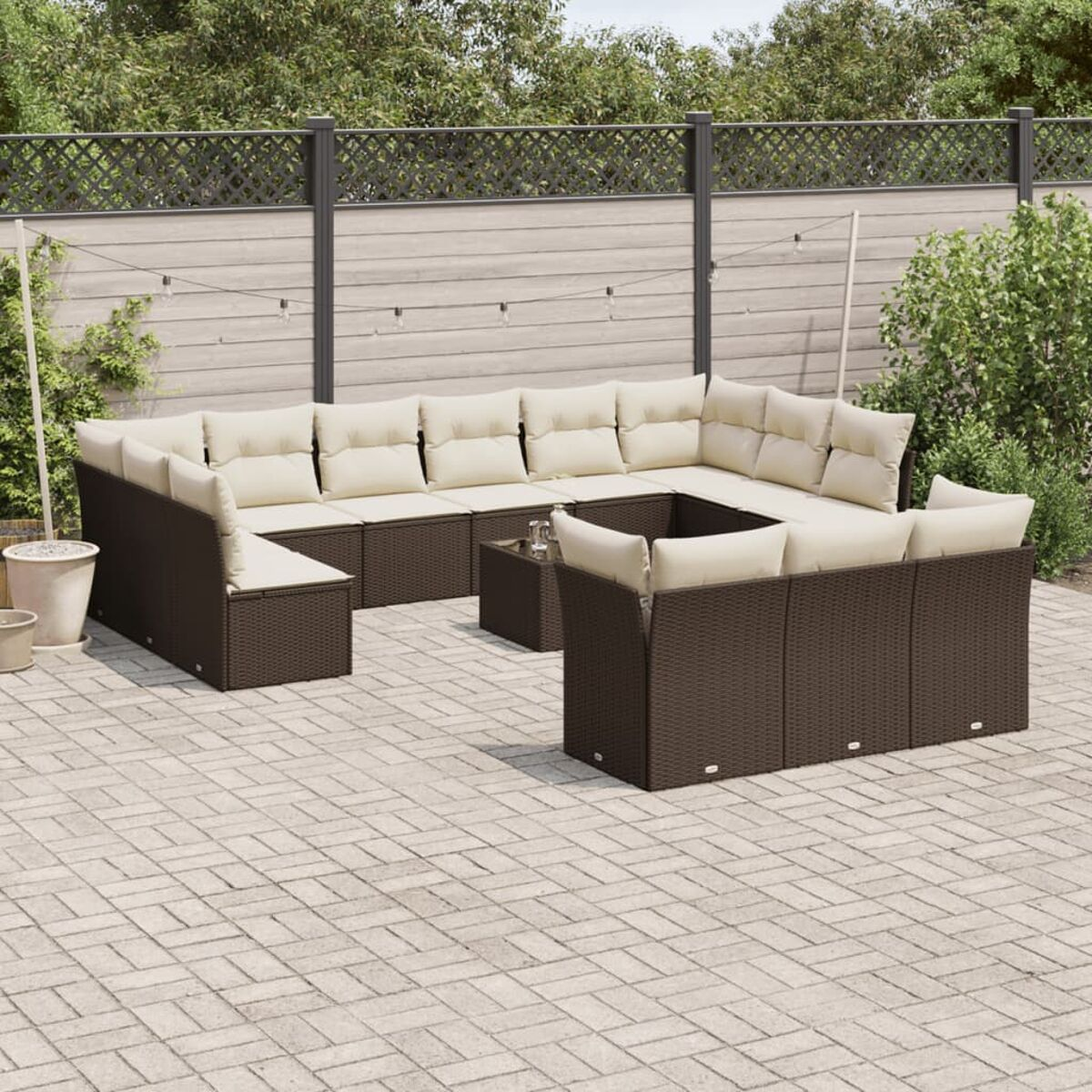 Divano angolare in vimini marrone scuro con cuscini color crema su un patio. Lo sfondo mostra un giardino.