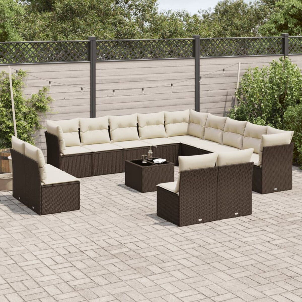Set di mobili da esterno in vimini marrone con cuscini color crema. Include divano componibile, sedie e tavolo.